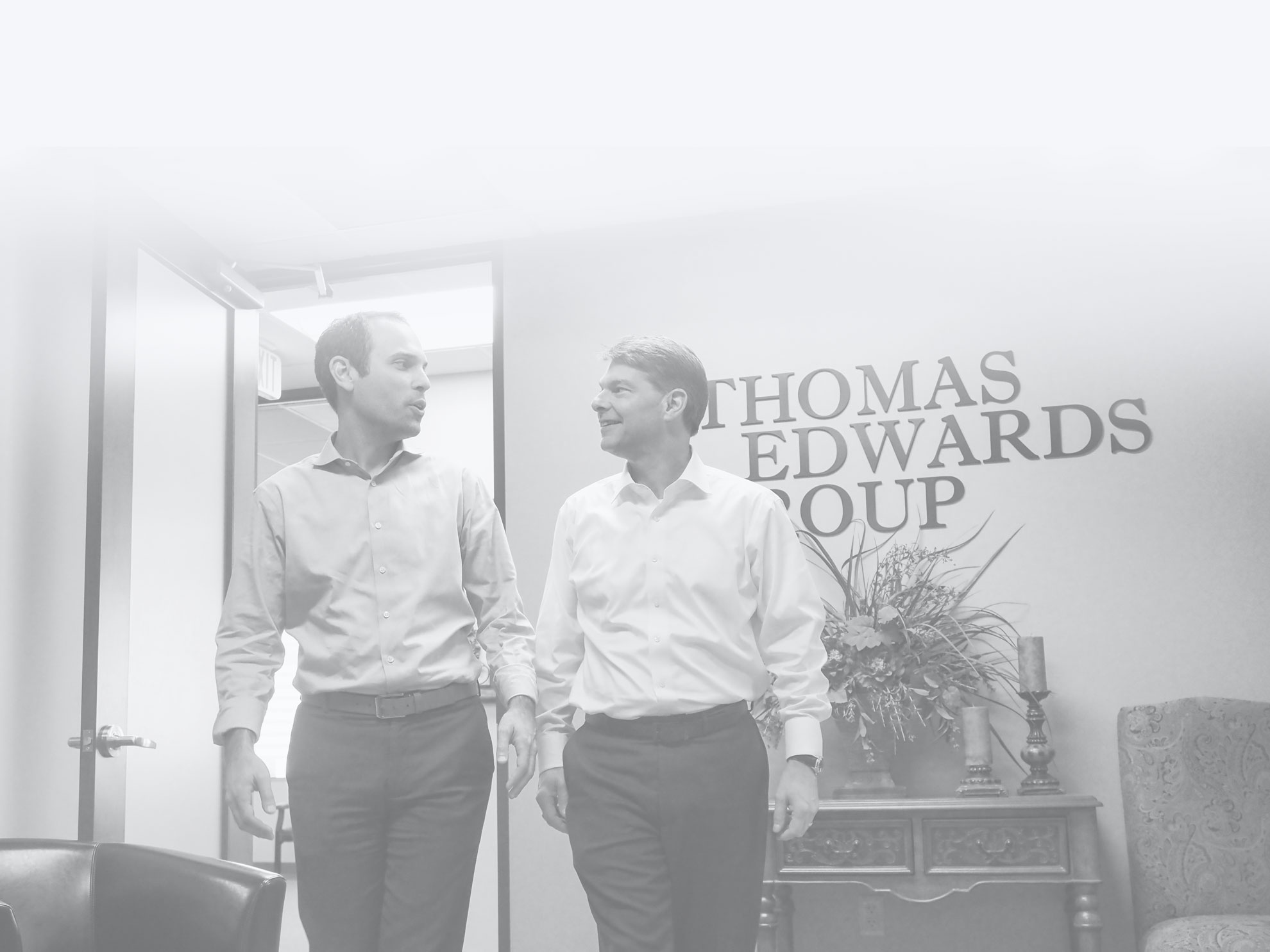 two professional men walking and talking in front of thomas edwards sign in office setting