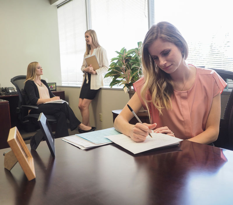 Thomas Edwards Group employees woman in pink shirt writing as co workers talk in background